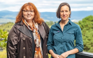 Dr Michelle Freeman and Jacquie Martin of Forestry Australia standing at a lookout with native forest and mountain ranges behind them.