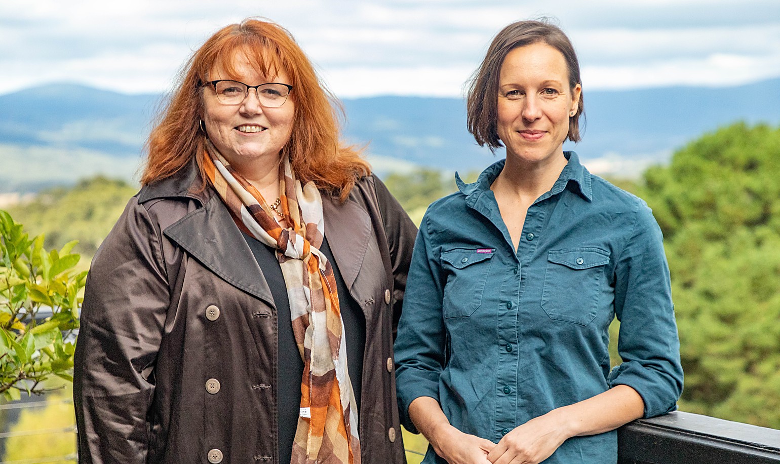 Dr Michelle Freeman and Jacquie Martin of Forestry Australia standing at a lookout with native forest and mountain ranges behind them.