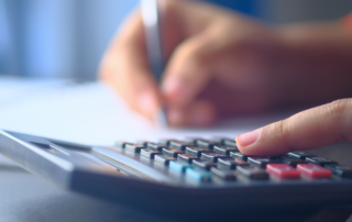 A hand pressing keys on a calculator while writing figures on paper.