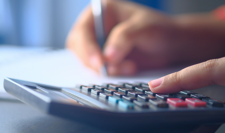 A hand pressing keys on a calculator while writing figures on paper.